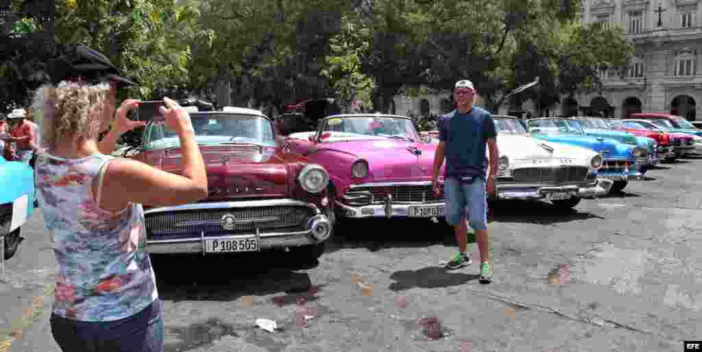 Turistas se toman fotos junto a varios autos clásicos en una calle de La Habana.