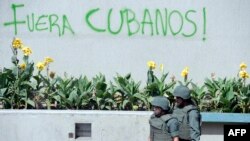 Miembros de la Guardia Nacional caminan delante de un cartel "Fuera Cubanos" en la Plaza Altamira de Caracas.