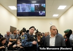 Alexei Navalny y Daniel Kholodny, director técnico de su canal de YouTube, aparecen en una pantalla de TV desde prisión durante una audiencia este martes en el tribunal de apelaciones en Moscú. (REUTERS/Yulia Morozova)