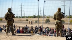 Migrantes esperan junto a una valla fronteriza bajo la vigilancia de la Guardia Nacional de Texas el 10 de mayo de 2023 para ingresar a El Paso, Texas. (AP/Andrés Leighton)