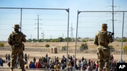 Migrantes esperan junto a una valla fronteriza bajo la vigilancia de la Guardia Nacional de Texas, el 10 de mayo de 2023, para ingresar a El Paso. (AP/Andrés Leighton)