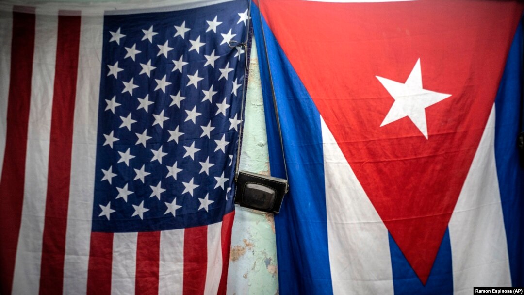 Banderas de Estados Unidos y Cuba cuelgan de una pared con una vieja cámara fotográfica colgada en el medio en La Habana, Cuba, el lunes 11 de enero de 2021. (Foto AP/Ramón Espinosa)