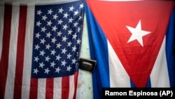 Banderas de Estados Unidos y Cuba cuelgan de una pared con una vieja cámara fotográfica colgada en el medio en La Habana, Cuba, el lunes 11 de enero de 2021. (Foto AP/Ramón Espinosa)
