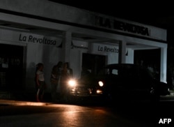 La gente usa un automóvil para iluminarse en una calle oscura durante un apagón en el municipio de Bauta, provincia de Artemisa, Cuba, el 18 de marzo de 2024. (Foto de YAMIL LAGE / AFP)