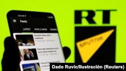 La app de RT en un teléfono móvil delante de los logos de RT y Sputnik. REUTERS/Dado Ruvic/Ilustración
