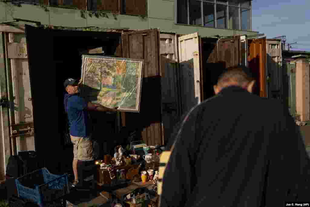 Pavel Sheludko muestra uno de los cuadros que vende a un comprador en un mercado callejero en Kyiv, Ucrania, el 9 de julio de 2023. 