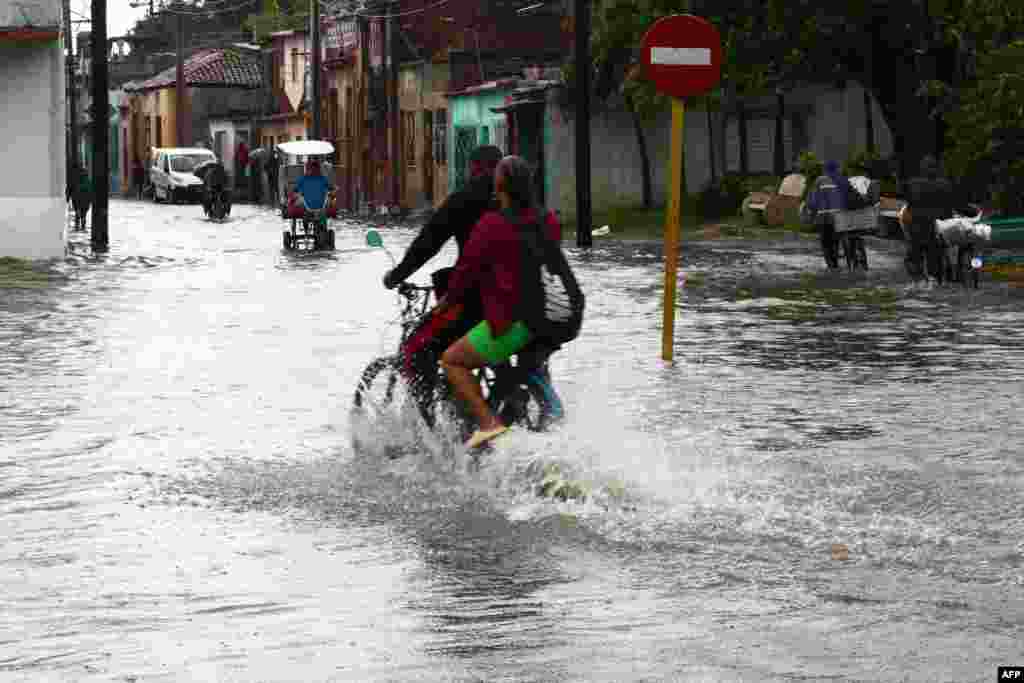 Personas pasean en motocicleta por una calle después de que las fuertes lluvias provocaran una inundación en Camagüey, Cuba