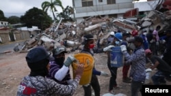 Equipos de rescate pasan escombros en cubos mientras revisan los restos tras los terremotos del 24 de junio, en La Guaira, Venezuela.