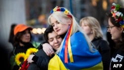 Dos mujeres envueltas en una bandera ucraniana se abrazan durante un flash mob en protesta por el abuso sexual de soldados rusos en Ucrania. (AFP/Kena Betancur).