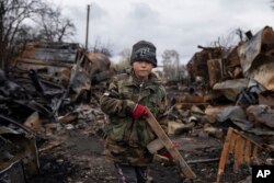Yehor, de 7 años, de pie con un rifle de madera junto a vehículos militares rusos destruidos cerca de Cherníhiv, Ucrania, el domingo 17 de abril. (AP/Evgeniy Maloletka)