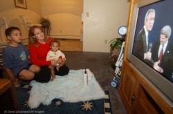La votante de Denver Teresa Natale, sosteniendo a su bebé y con su hijo de 6 años, ve un debate presidencial de 2004. (© David Zalubowski/AP Images)