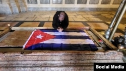 El sacerdote Kenny Fernández Delgado ora frente a una bandera cubana. (Foto: Facebook)