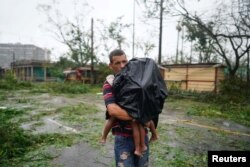 Un hombre lleva a sus hijos junto a los escombros causados por el huracán Ian después de su paso en Pinar del Río, Cuba.