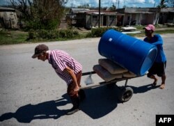 Hombres transportan un tanque de agua a lo largo de una calle en La Coloma, provincia de Pinar del Río. (Yamil Lage/AFP)