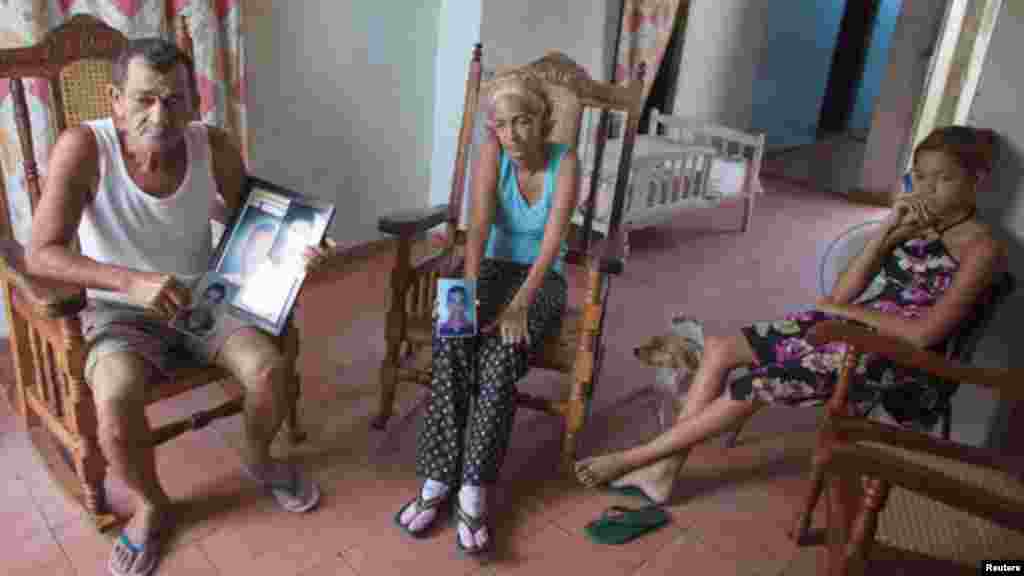Joaquín de La Paz, mecánico (izquierda) y su esposa Xiumara Milán Montero (centro), sentados con uno de sus nietos, sostienen fotografías de dos de sus hijos y dos de sus otros nietos que recientemente murieron tratando de llegar a Honduras en un improvisado barco. 
