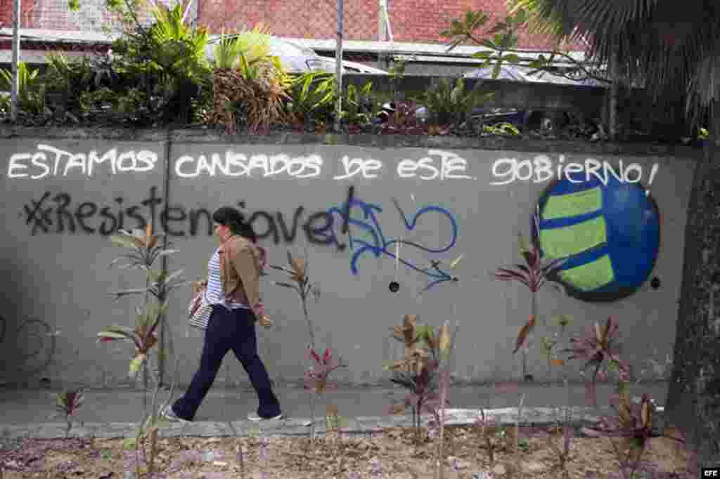 Una mujer pasa frente a una pared con mensajes de protesta contra el gobierno de Venezuela hoy, lunes 16 de febrero de 2014, en el sector El Cafetal en Caracas.
