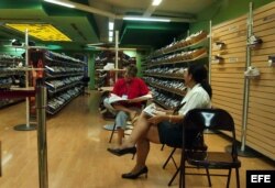 Dos empleadas leen el periódico en una ociosa tienda de calzado deportivo ubicada en el Centro Comercial Carlos III.