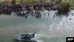 Un barco de la Patrulla Fronteriza de EEUU pasando a un gran grupo de migrantes que esperan cruzar la barrera de alambre de púas hacia los Estados Unidos, en Eagle Pass, Texas, el 25 de septiembre de 2023.