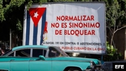 Un auto pasa junto a un cartel alusivo al embargo estadounidense a Cuba.