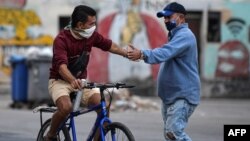 Dos hombres se estrechan la mano en una calle de La Habana, en medio de una ola de contagios de coronavirus. (YAMIL LAGE / AFP)