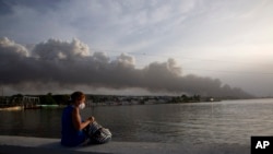 Una mujer contempla desde el malecón el humo del incendio en la Base de Supertanqueros de crudo en la Bahía de Matanzas, este martes, 9 de agosto. (AP Foto/Ismael Francisco)