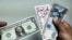 Un hombre muestra un dólar estadounidense y pesos cubanos. (YAMIL LAGE / AFP)