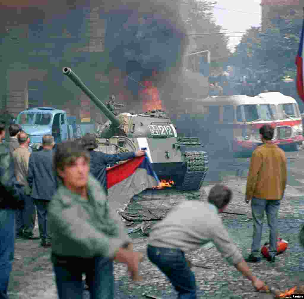 No mucho después de tomada la foto anterior, dijo Hajsky, la situación en torno a Radio Checoslovaca descendió al caos. &quot;Algunos muchachos lograron agarrar las palas que tenían en los tanques y perforaron los barriles [de combustible]&quot;, dice. &quot;Y les prendieron fuego con paños empapados en diesel. Y con el humo, se puede ver cómo las calles se oscurecieron como si fuera de noche. Y poco a poco, la metralla comenzó a volar también. Hubo un terrible pánico. La gente se cubrió donde pudo - detrás de los autos, en el suelo&quot;.