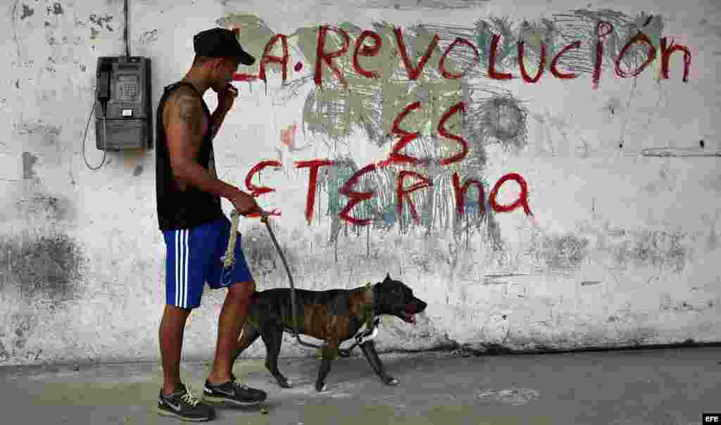 Un joven pasea con su perro junto a un cartel alusivo a la Revolución Cubana en una calle de La Habana.