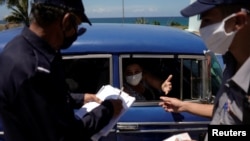 La policía revisa el lunes los documentos de los pasajeros de un auto en el punto de control de Boca de Jaruco, en Mayabeque, antes de remitirlos al personal sanitario que les tomará la temperatura (Alexandre Meneghini/Reuters).