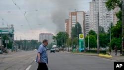 Un hombre cruza la calle mientras una columna de humo sale del fondo, en Kiev, Ucrania, el domingo 5 de junio de 2022. (AP Foto/Natacha Pisarenko)