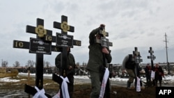 Trabajadores en un cementerio colocan cruces en las tumbas de cinco miembros de una familia que fallecieron tras un ataque ruso con drones en Kharkiv, el 12 de febrero de 2024. (AFP/Sergey Bobok).
