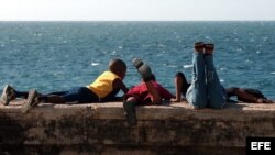 Una madre con sus hijos observa el mar, hoy martes 18 de mayo, desde el muro del malecón habanero al atardecer. 