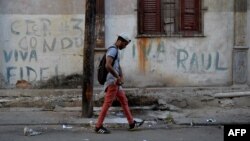 Un hombre camina frente a un muro en el que han escrito "Viva Fidel; Viva Raúl". 