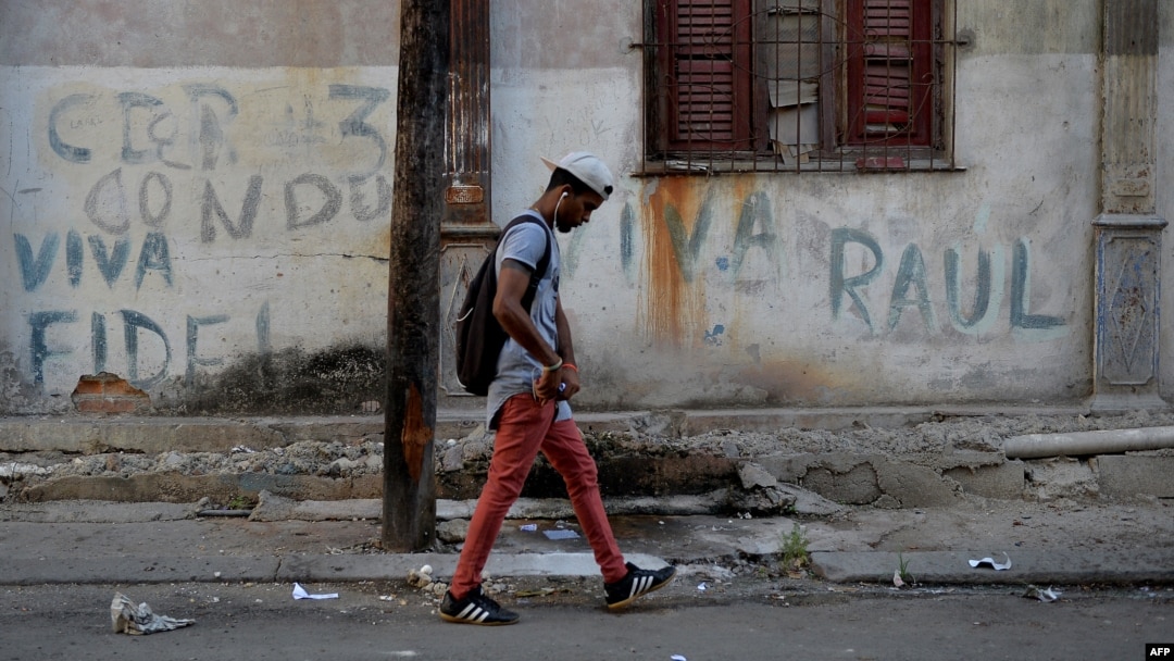 Un hombre camina frente a un muro en el que han escrito "Viva Fidel; Viva Raúl". 