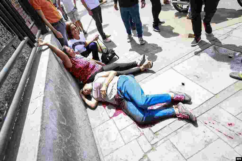 os mujeres yacen en el suelo durante un enfrentamiento entre un grupo de personas adeptas al oficialismo y personas opositoras.
