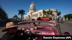 Un clásico auto estadounidense convertido en taxi de turismo pasa frente al Capitolio de La Habana. Foto: AP/ Ramón Espinosa
