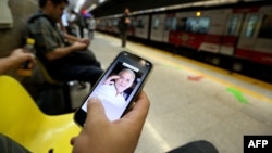 Un iraní en su teléfono celular con una imagen del candidato presidencial ganador Masoud Pezeshkian, mientras espera su tren en una estación de metro en Teherán el 6 de julio de 2024, el día después de que la nación celebrara elecciones presidenciales.