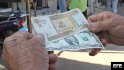 Un hombre muestra un peso convertible cubano y un dólar estadounidense frente a una oficina de la Western Union en La Habana (Cuba).