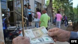 Un hombre muestra un peso convertible cubano y un dólar estadounidense frente a una oficina de la Western Union en La Habana.