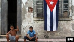 Dos niños posan para una fotografía al frente de una casa con la bandera cubana.