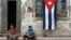 Dos niños posan para una fotografía al frente de una casa con la bandera cubana.