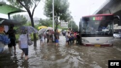 Varias personas tratan de subir a un autobus en una carretera inundada en Tianjín, al norte de China, hoy jueves 26 de julio de 2012. La reciente oleada de aguaceros han matada a más de 100 personas en China. EFE/Geno Zhou PROHIBIDO SU USO EN CHINA