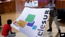 Empleados con un cartel con el logo de Telesur, en la sede de la televisora en Caracas. (AP Photo/Leslie Mazoch,File)
