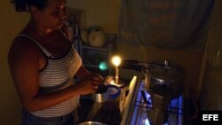 Una mujer prepara unos platos de comida en la cocina, iluminada con velas, durante un apagón en el barrio de Alamar.
