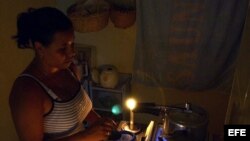 Una mujer prepara unos platos de comida en la cocina, iluminada con velas, en un apagón en el barrio de Alamar