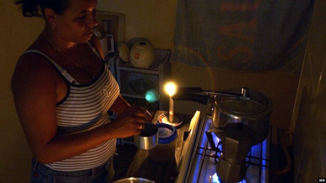Una mujer prepara unos platos de comida en la cocina, iluminada con velas, durante un apagón en el barrio de Alamar.