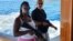 John McAfee junto a una mujer en su yate, sosteniendo armas de asalto. (Twitter/@officialmcafee)