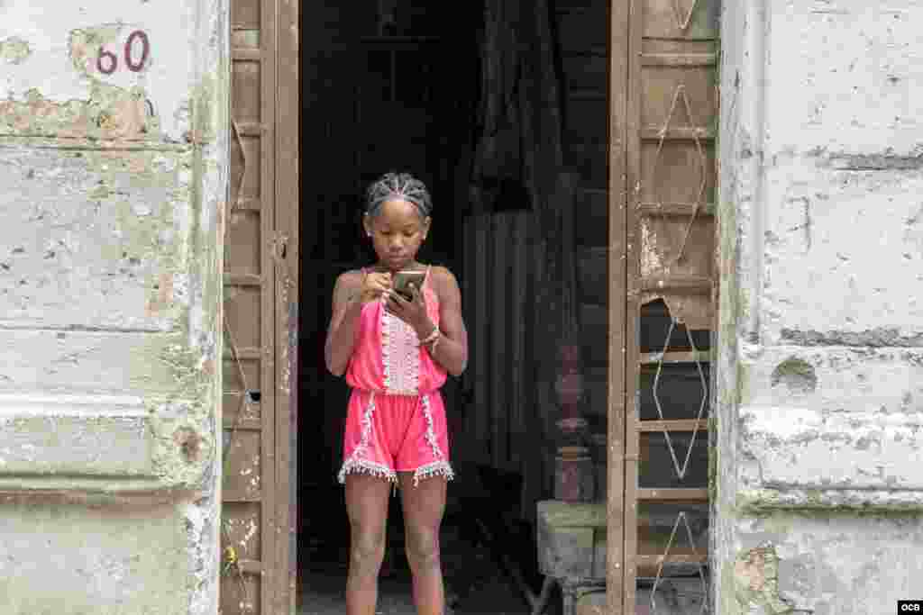 Niña en Cuba usando el celular en el portal de su casa.