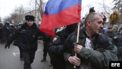 Agentes antidisturbios arrestan a un activista con una bandera nacional rusa