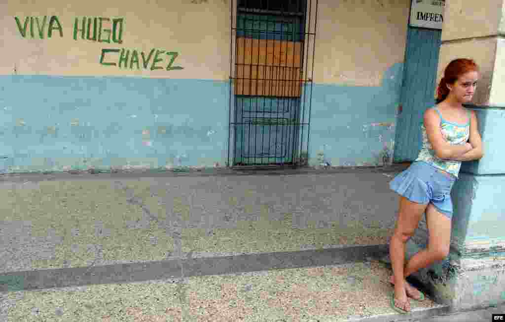 Una mujer barre la calle frente a un cartel del ALBA.